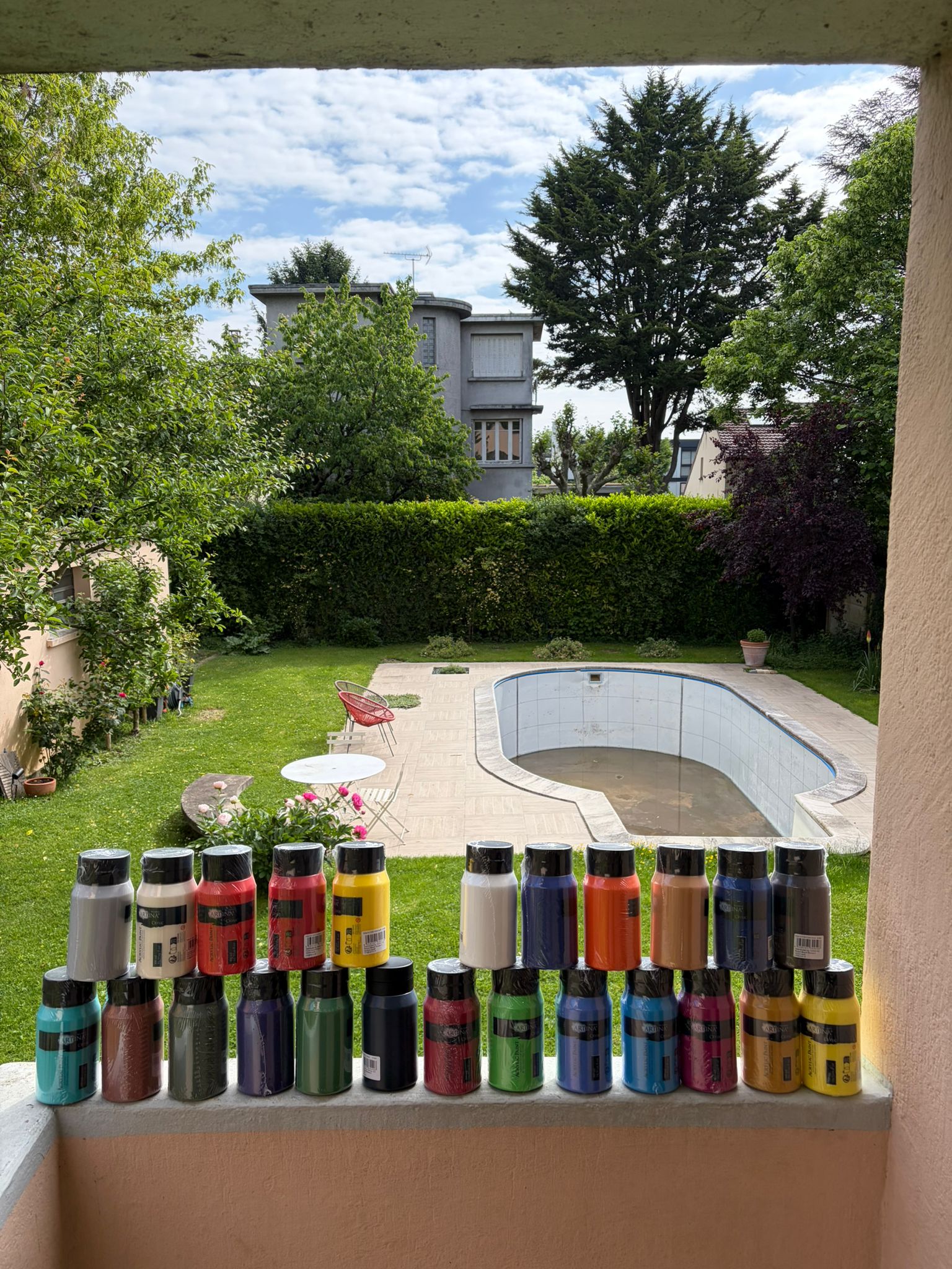 Les trente pots de peinture prêts pour l'atelier — piscine vide visible en arrière-plan
